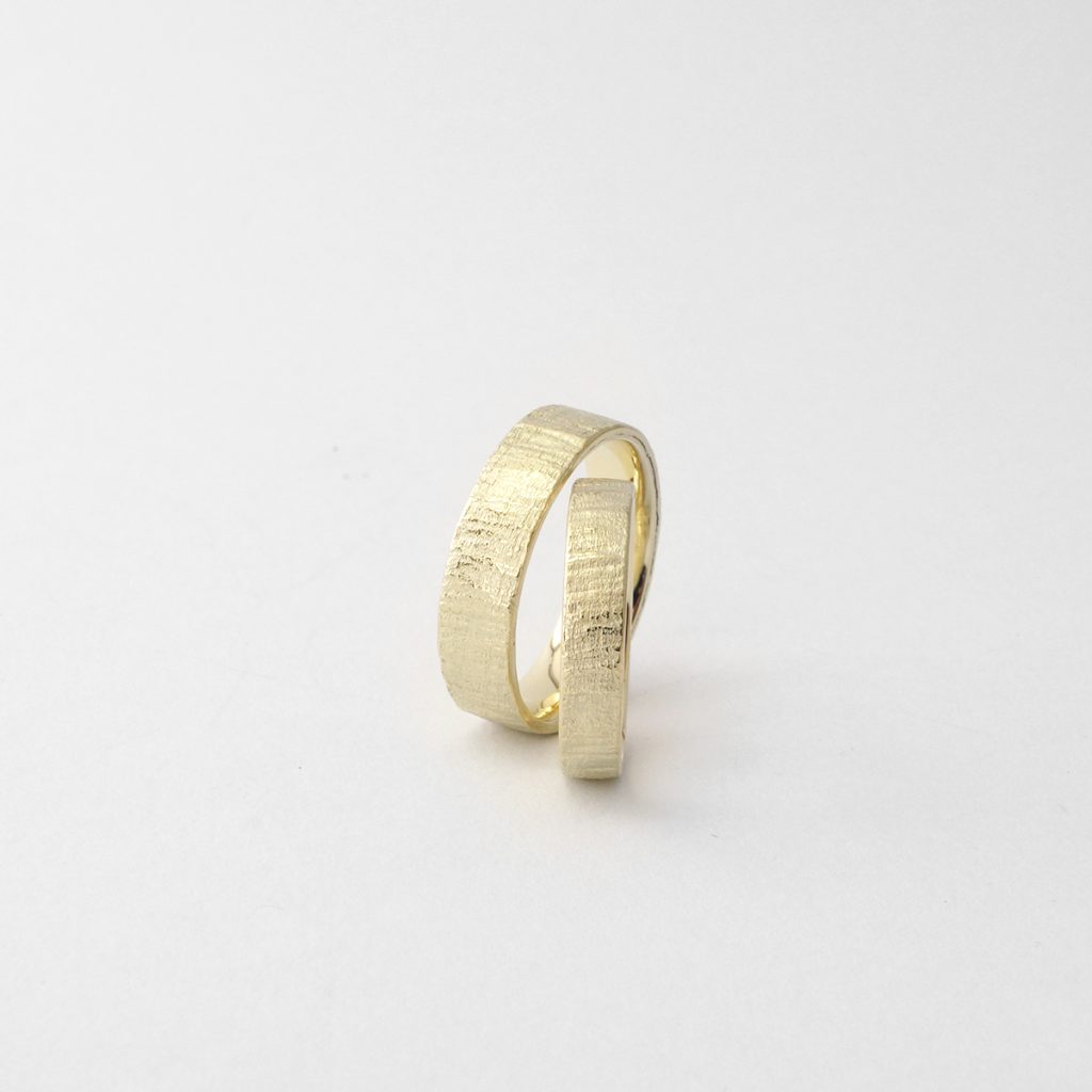 Paar Trauringe in Gelbgold mit Holzstruktur handgemacht.